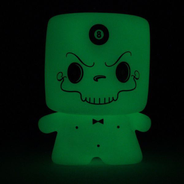Limited edition Grim Marshall by 64 Colors (Squibbles Ink + Rotofugi): A green, glowing marshmallow-like toy figure with a skull face, mustache, bow tie, and 8-ball on its forehead shines against a black background.
