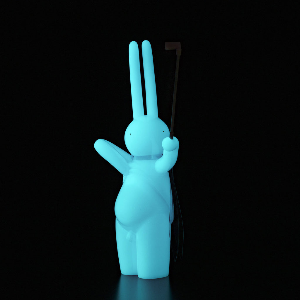 The Daily Flasher by mr. clement from Tomenosuke Shoten is a glowing blue, rabbit-shaped vinyl figure standing upright with a black stick in one hand, shown against a black background.