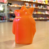 The Popsoda Finger Puppet - Orange by Pop Soda features spiky details and sits on a smooth surface, facing away from the camera, with blurred colorful shelves in the background. A fun addition to any Pop Soda finger puppets collection.