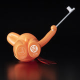 The Daily Flasher by mr. clement, from Tomenosuke Shoten, is an orange plastic device with a retractable metal hook and bilingual labeling in Japanese and English, shown on a black surface—resembling a sofubi collectible.