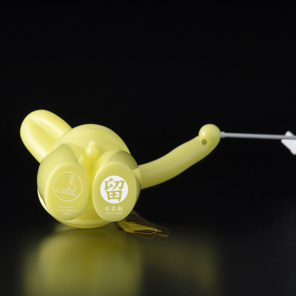 The Daily Flasher by mr. clement for Tomenosuke Shoten is a yellow plastic device with Japanese text, pictograms, a curved handle, and white cord, reflecting glow-in-the-dark vinyl toy culture. Photographed on a black background.