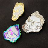 Three Rotofugi Pirate Abe Enamel Pins—head with eyepatch designs in gold, silver, and iridescent finishes—are displayed on black fabric. A unique accessory by Rotofugi for designer toy fans.