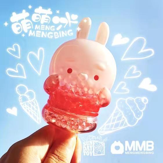 A hand holds the Meng Meng Bing — Bunny Popsicle Mini-Figure by Sun Day Toy, featuring a translucent bunny filled with pink and clear beads. White hearts, ice cream cones, and popsicles decorate the light blue background.